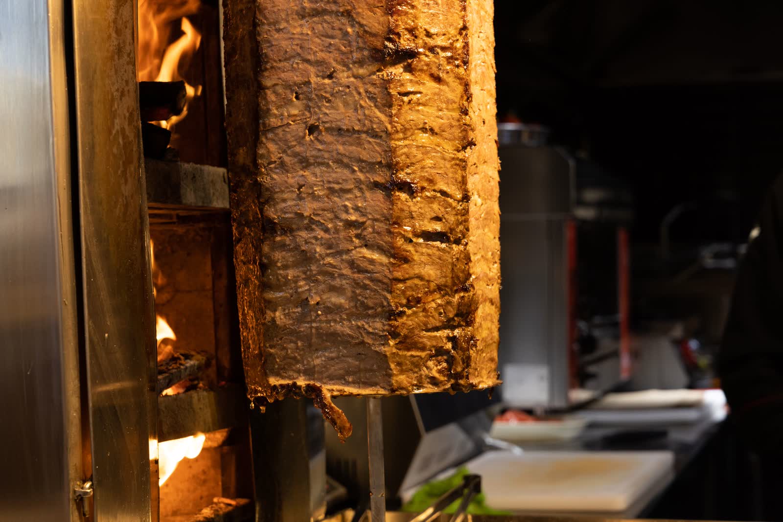 Een draaiende shoarmaspit met gebruind vlees, naast het vuur van de grill.